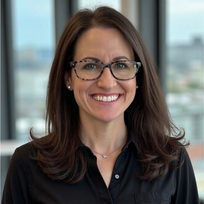Woman with glasses and brown hair smiling in an office setting.